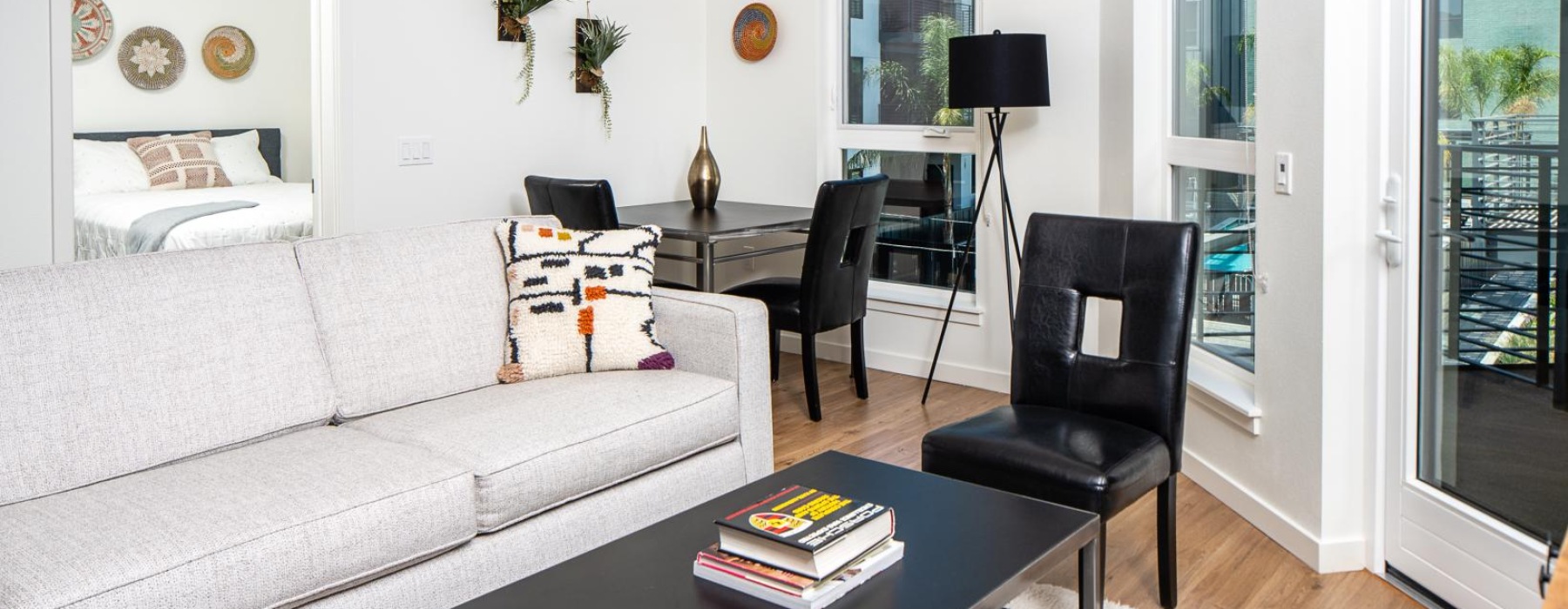 Bright modern apartment living area with a gray sofa, dining table, floor-to-ceiling windows, and balcony access.