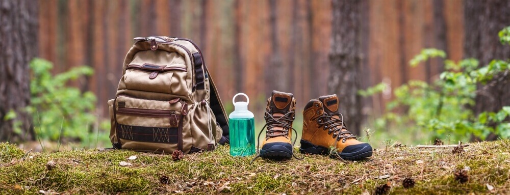 Backpack, hiking boots, and water bottle on a mossy forest floor.